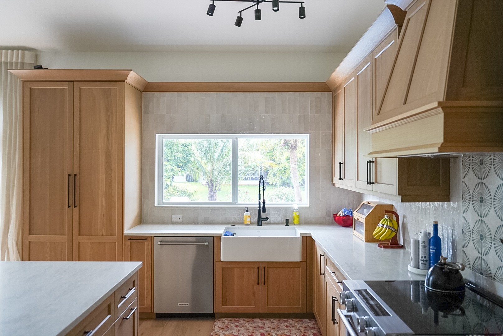 White oak kitchen run with farmhouse sink under the window, paneled dishwasher, and tall pantry cabinetry