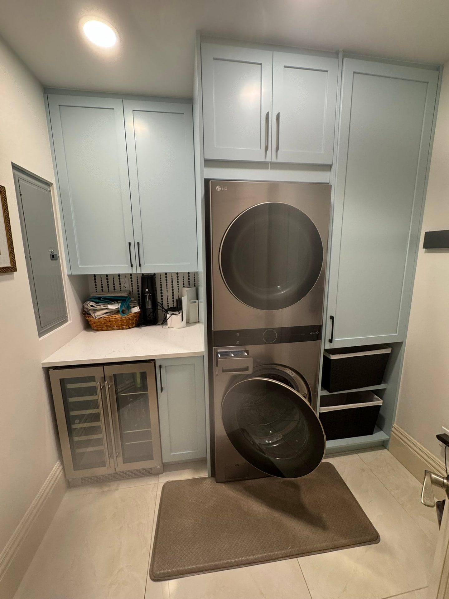 Custom light blue painted laundry room cabinetry with folding counter, tall storage cabinet, and stacked washer and dryer