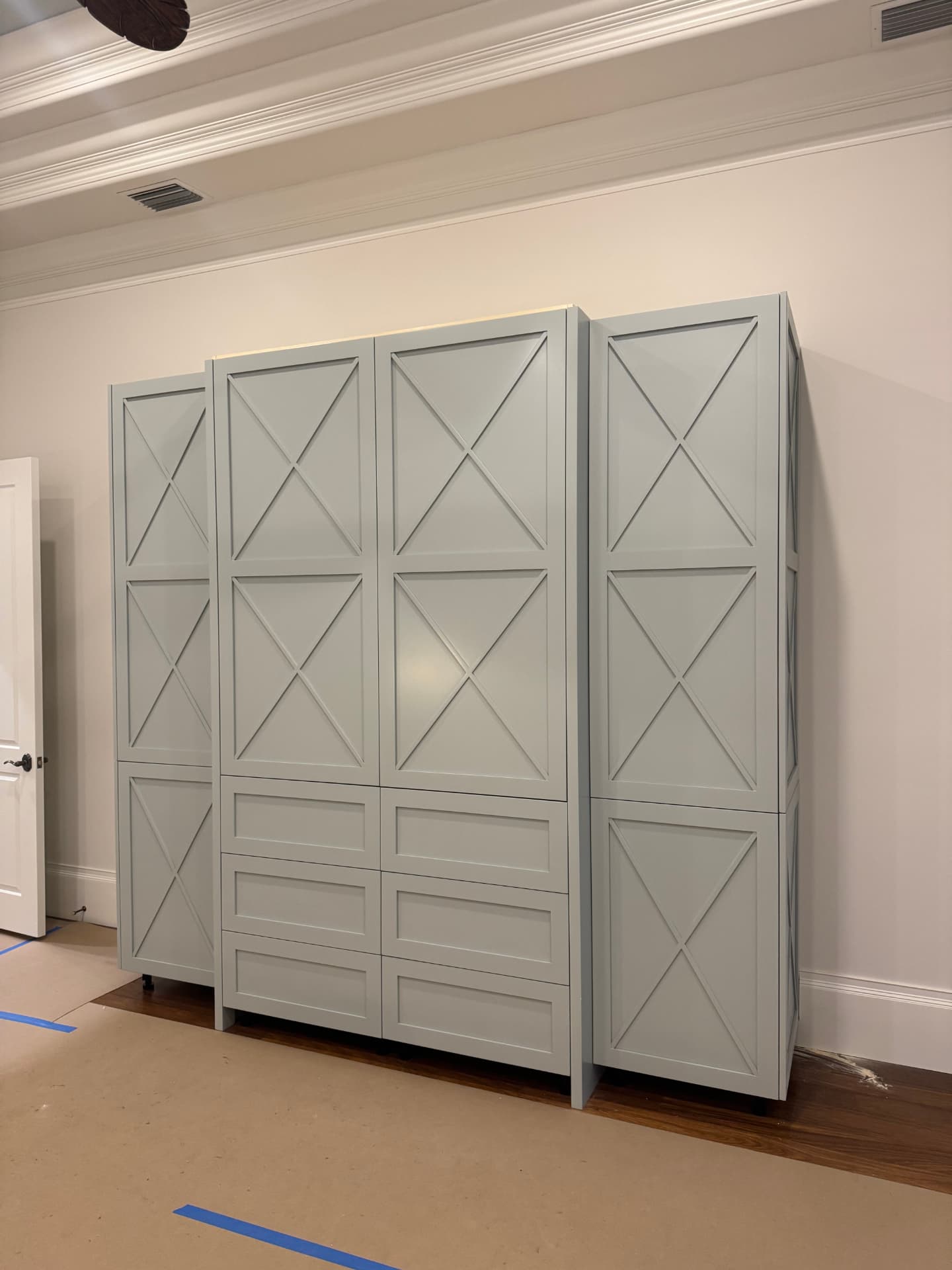 Painted X-panel built-in cabinet run with tall doors, center drawers, and stepped end cabinets