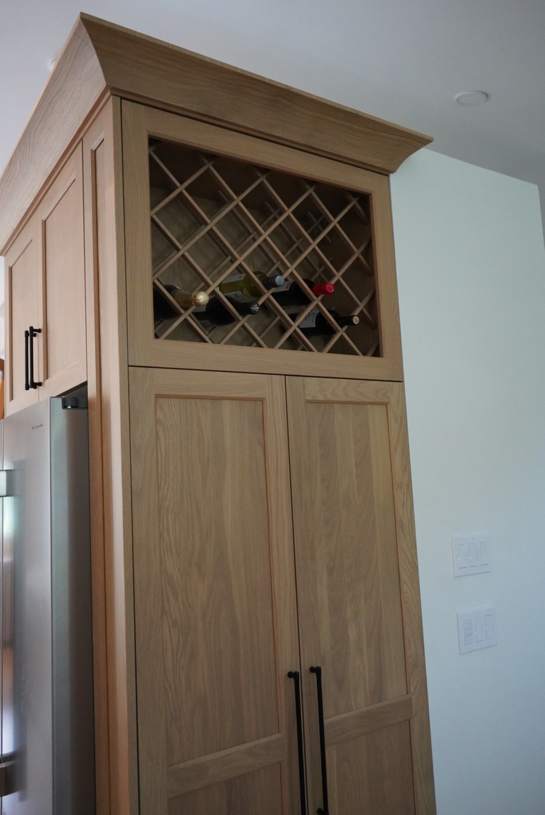 Detail of the oak wine bottle lattice cabinet above paneled refrigerator doors