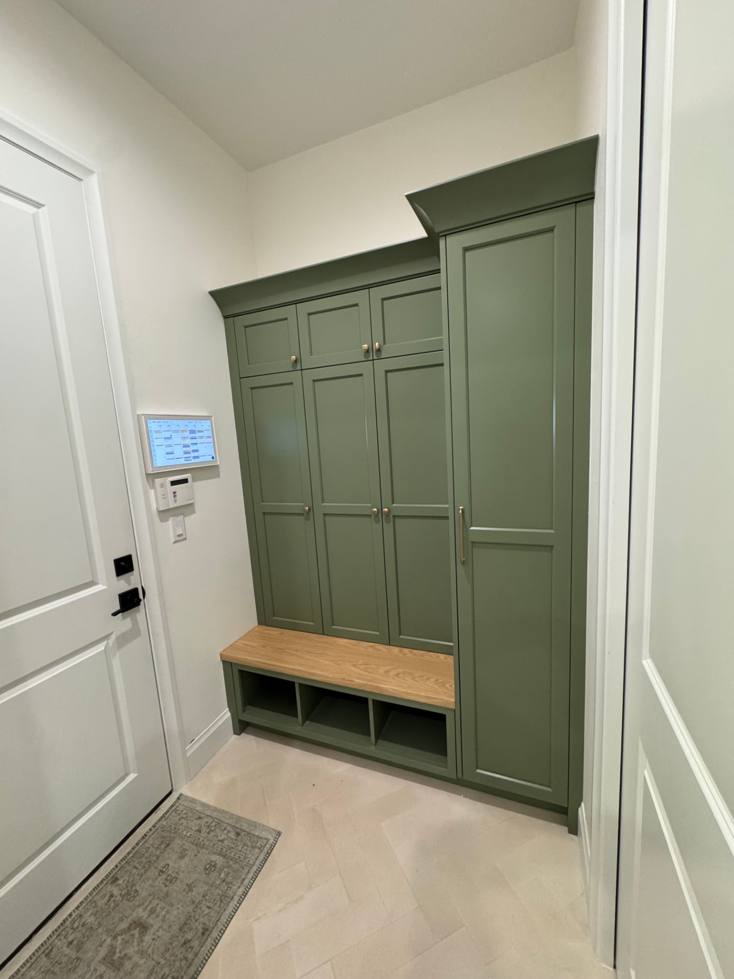 Sage green mudroom cabinetry with tall pantry-style storage beside the bench