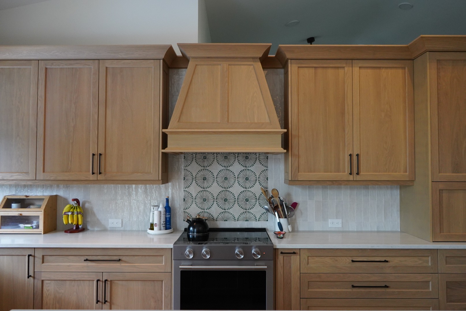 Close view of the custom white oak range hood above a stainless range with patterned backsplash tile