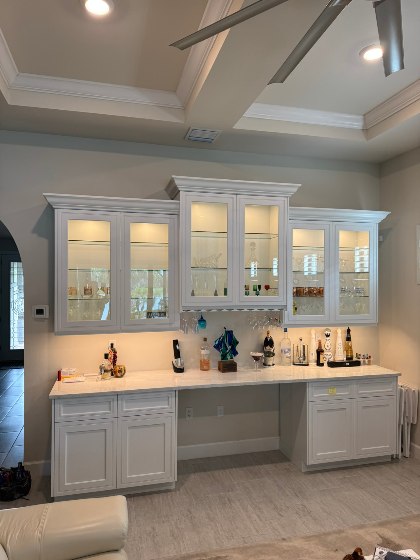 Custom painted dry bar with lit glass-front cabinets, glass shelving, and stone counter