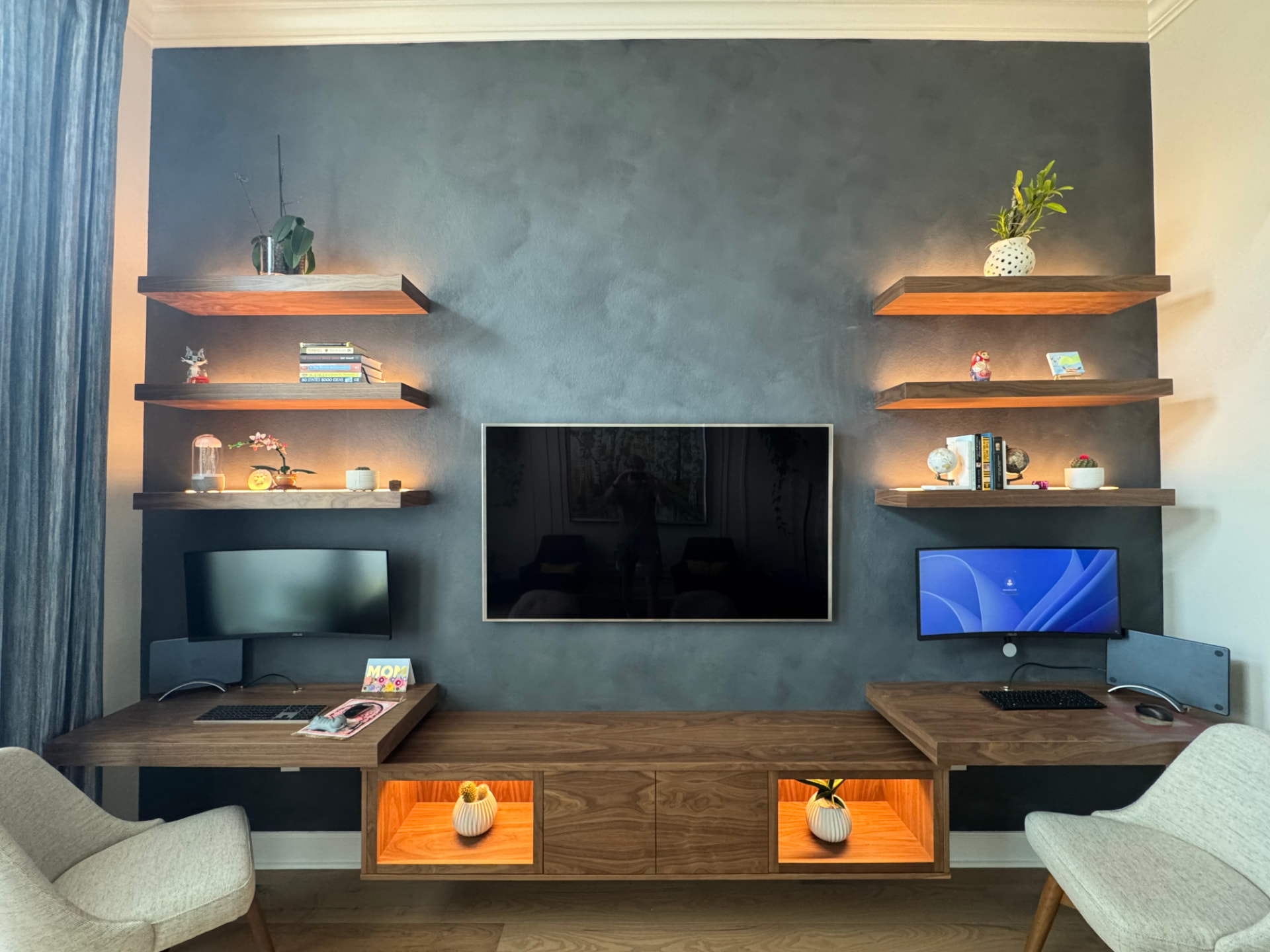 Custom floating walnut media wall with dual built-in desks, lit display niches, and floating shelves for a trade partner project