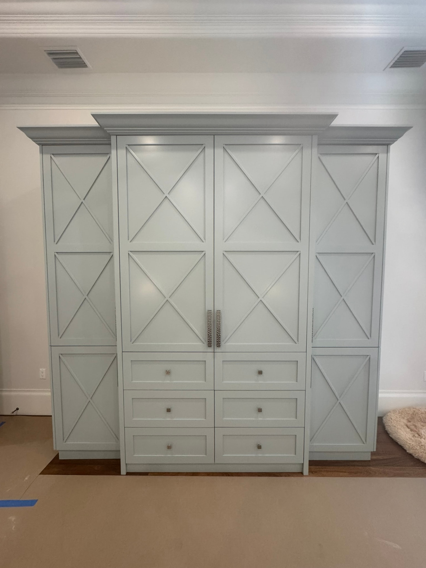Custom soft blue-green painted built-in cabinetry with X-panel doors, drawer bank, and crown molding