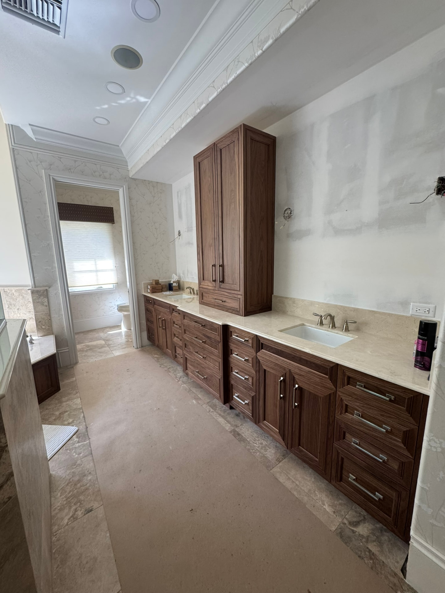 Long walnut double vanity with stone counters and a tall center storage cabinet