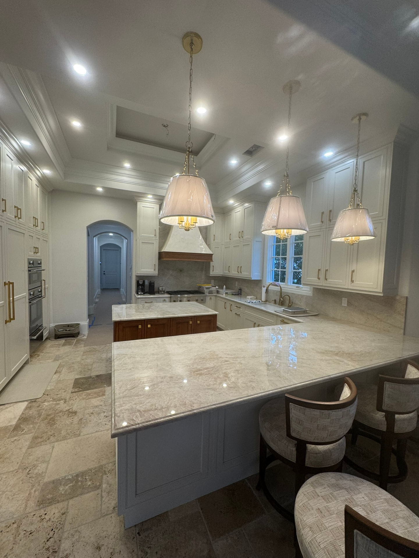 Wide view of the custom cream kitchen with paneled appliance cabinetry, brass hardware, and marble bar-height peninsula