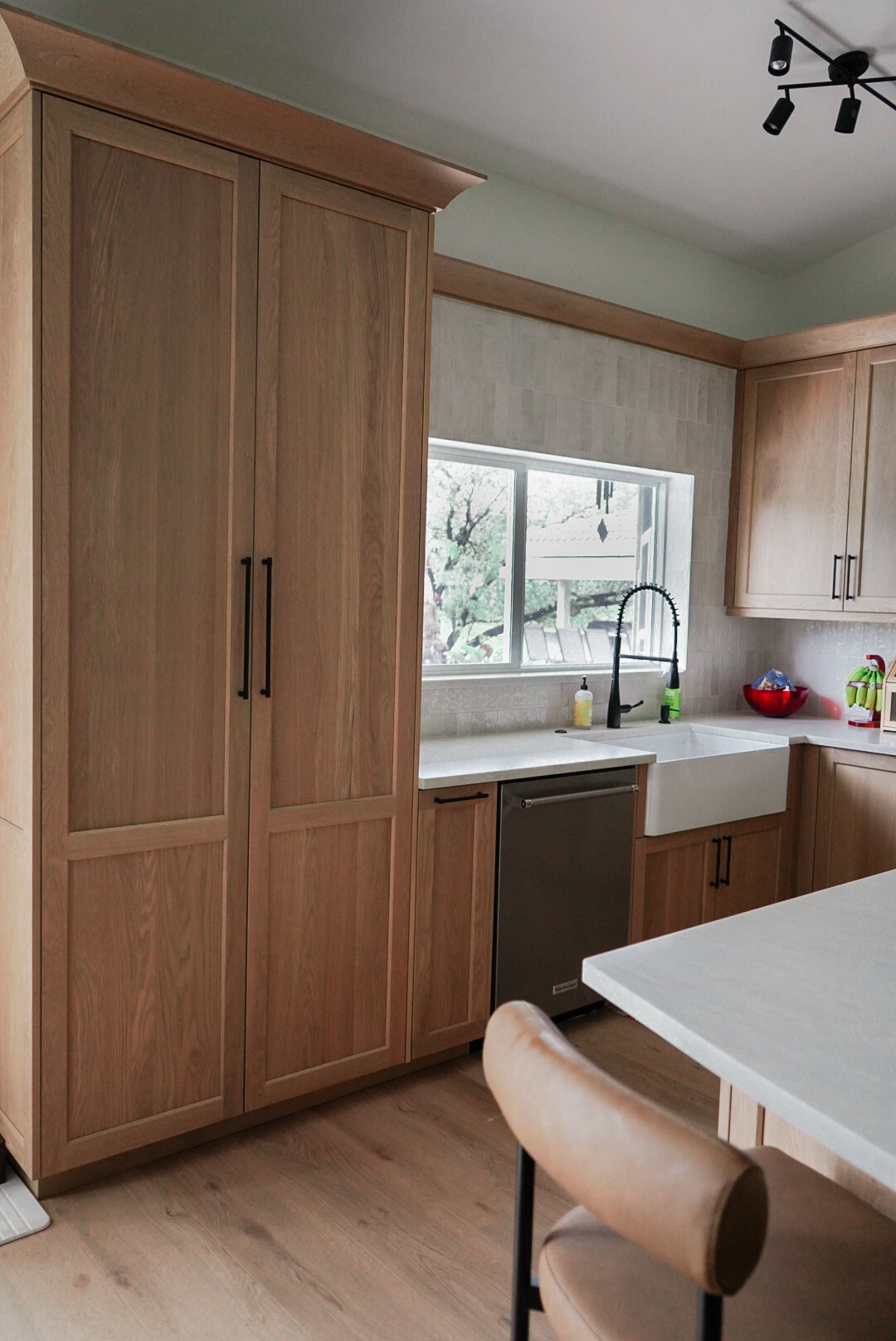 Tall white oak pantry cabinet beside the farmhouse sink corner of the kitchen