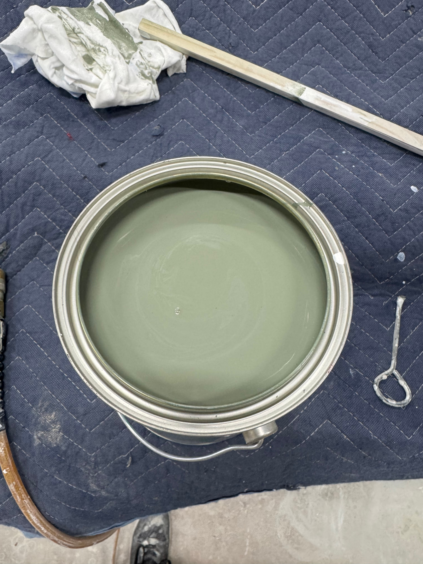 Open can of custom-matched sage green cabinet paint with a stir stick