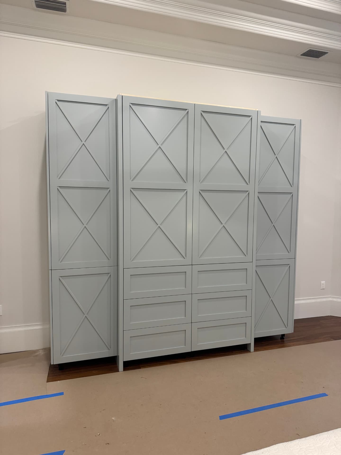 Custom soft gray-green painted X-panel built-in cabinetry with drawer bank and top light valance