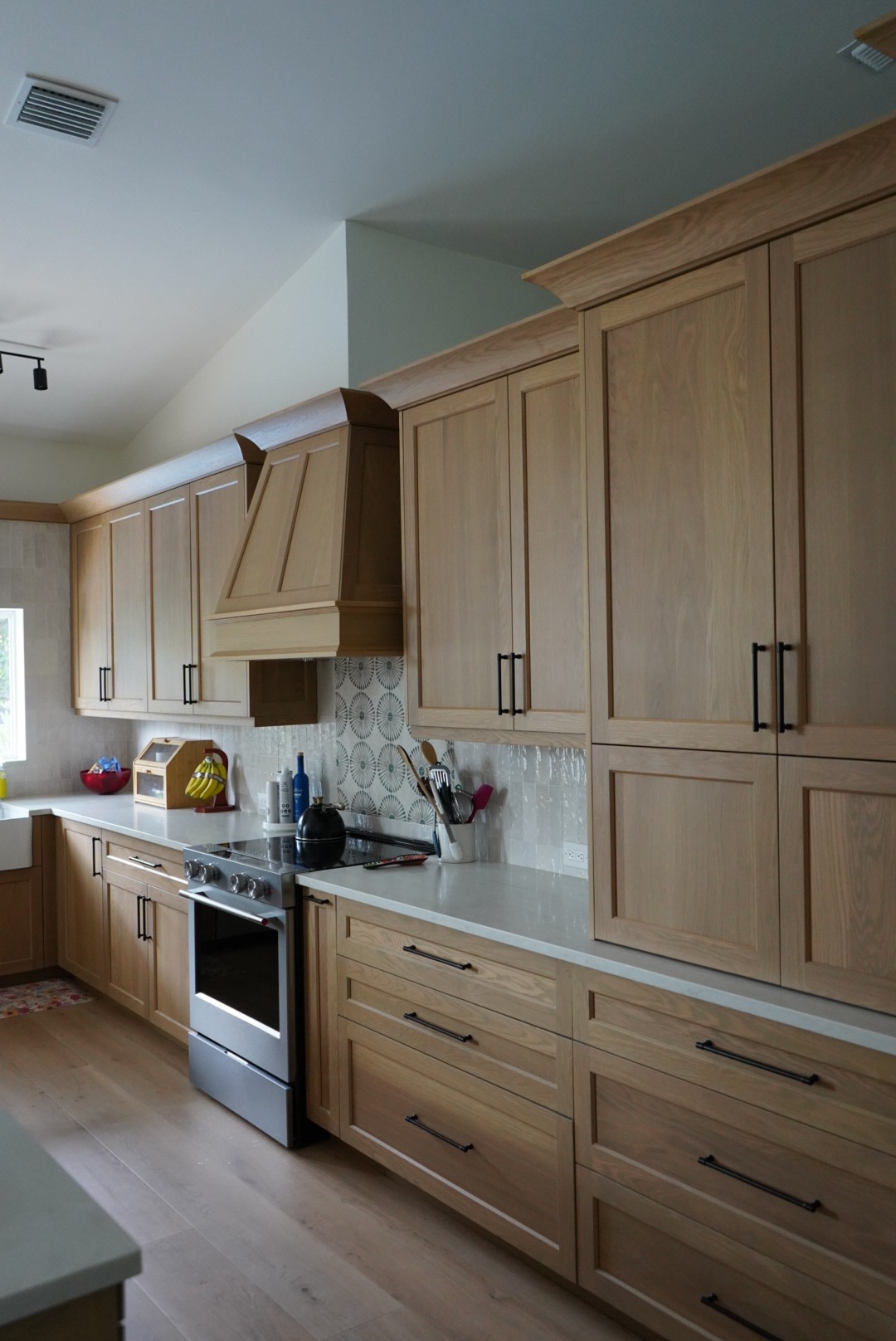 Range wall of the white oak kitchen with custom wood hood and tiled backsplash