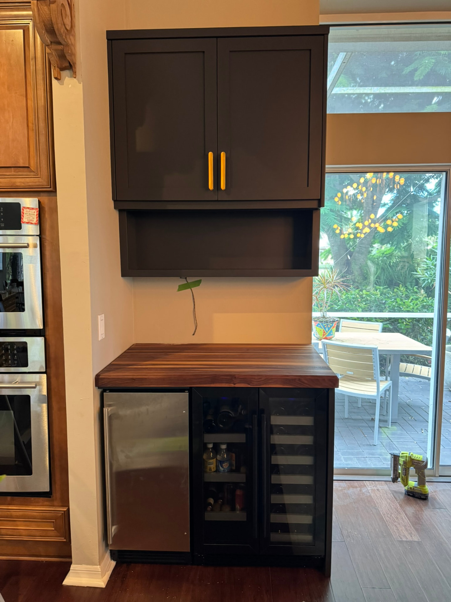 Dark painted bar cabinet with brass pulls, open shelf, and built-in beverage coolers
