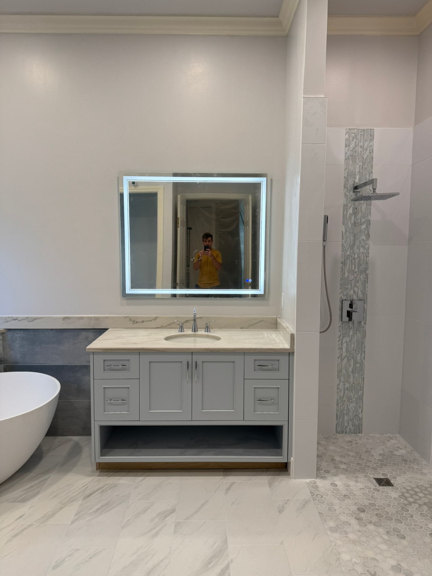 Painted gray vanity with open lower shelf beside a freestanding tub and tiled shower