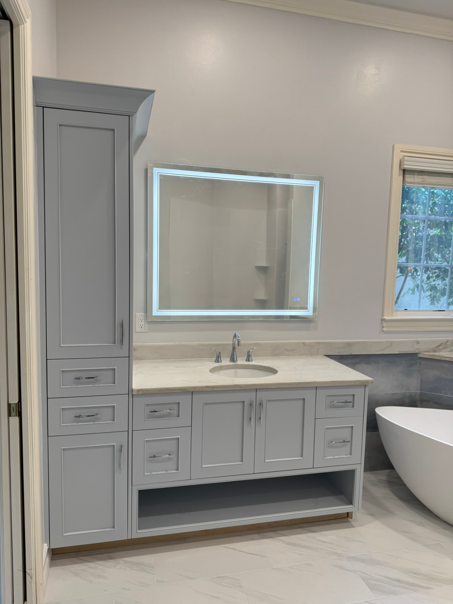 Custom painted gray bathroom vanity with marble counter and matching full-height linen tower