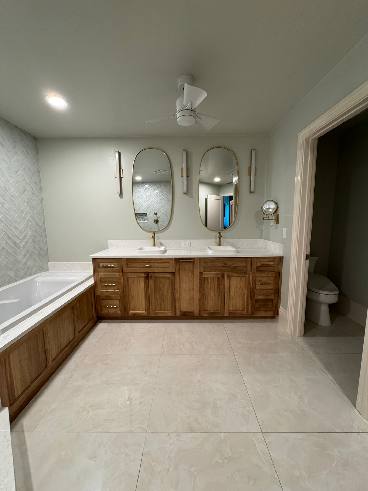 Walnut double vanity with matching paneled tub surround and oval mirrors