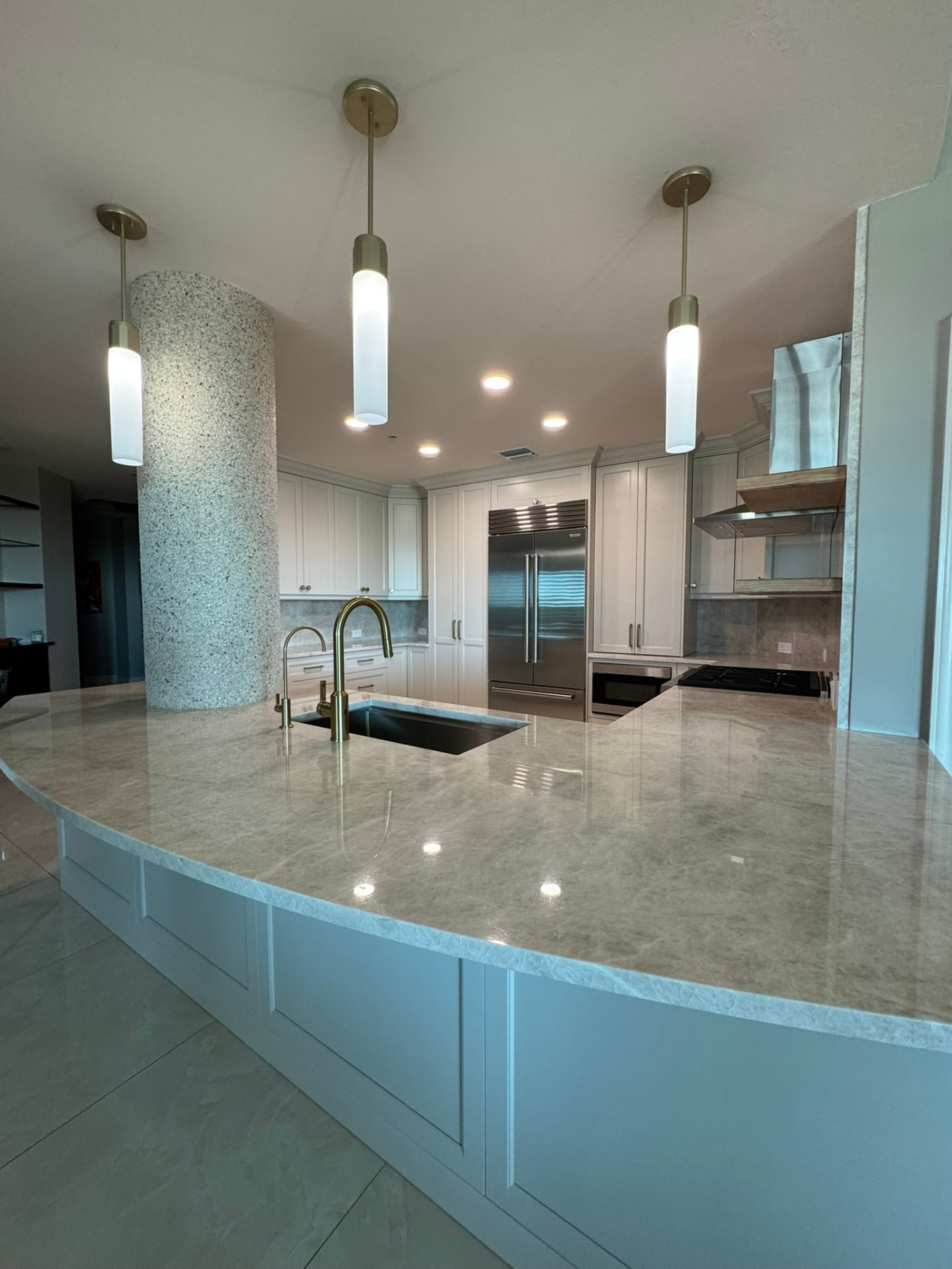 Curved quartzite peninsula with painted paneled base cabinetry and brass fixtures