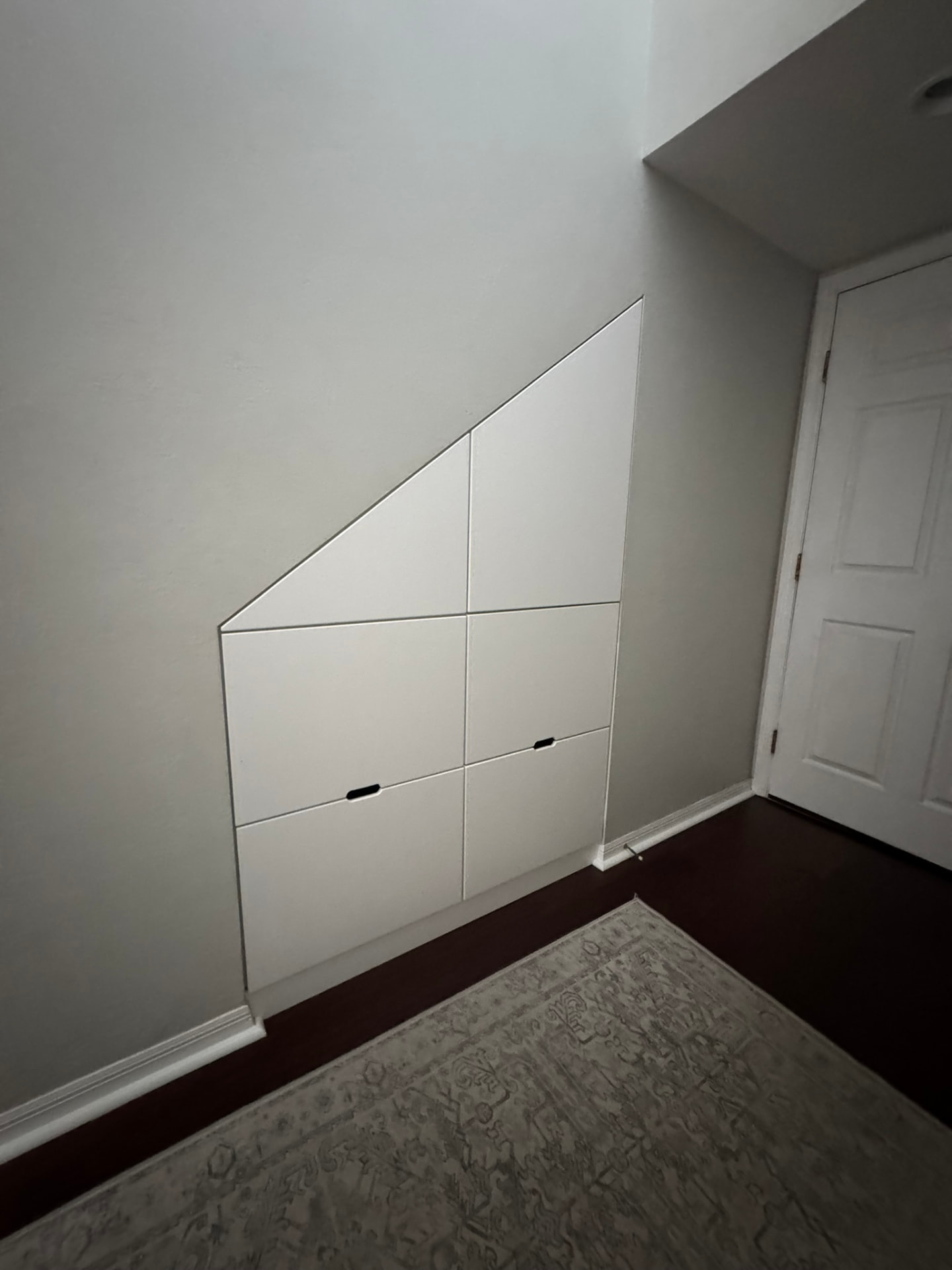 Custom under-stair storage cabinetry with angled flush panel doors and drawers