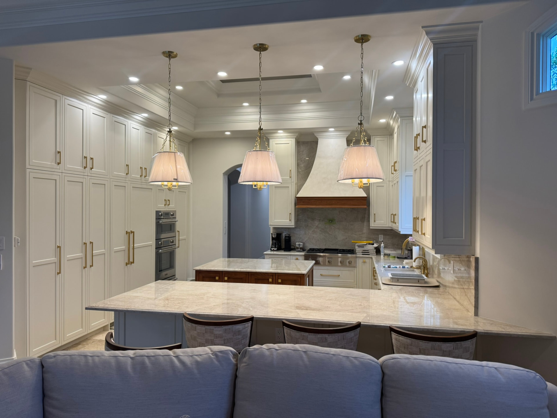 Custom cream painted kitchen with floor-to-ceiling cabinetry, plaster hood surround, walnut island, and marble peninsula counter
