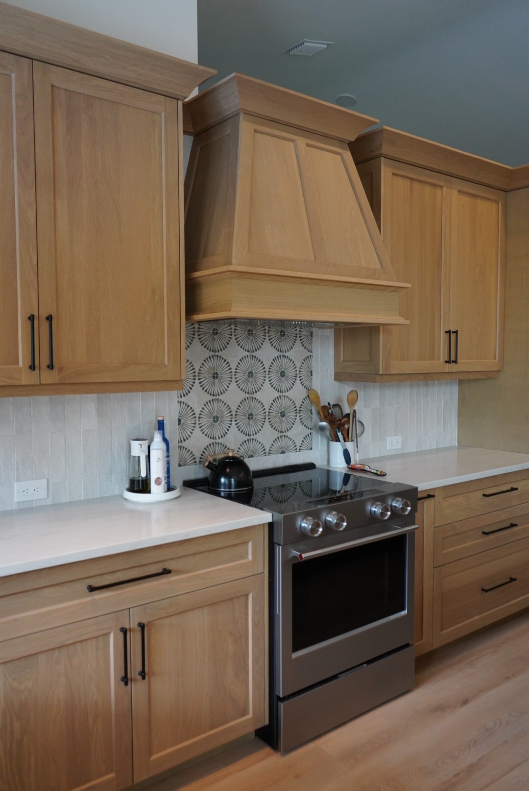Angled view of the white oak range hood, cabinetry, and backsplash in the kitchen