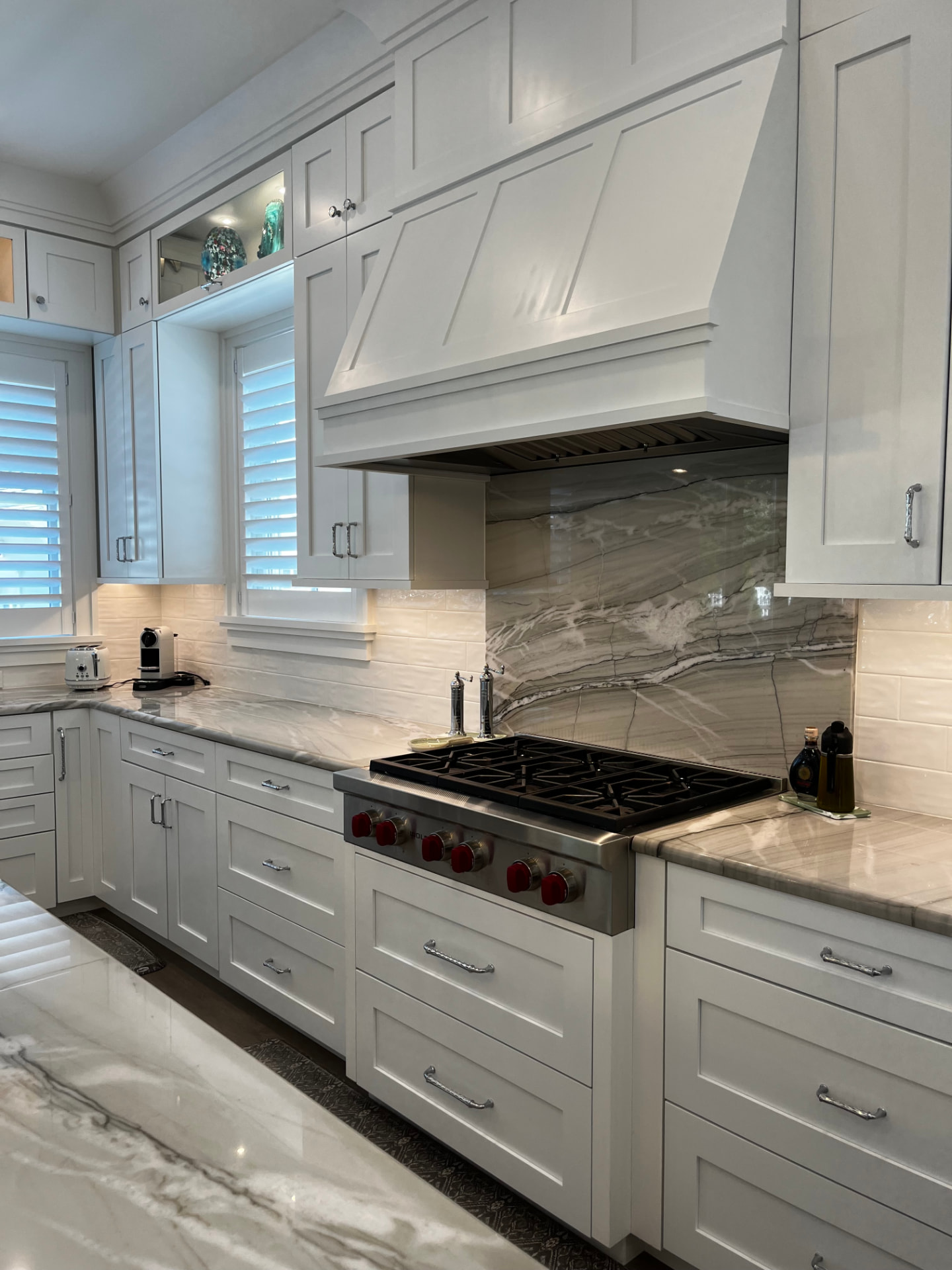 White shaker range wall with a paneled custom hood, quartzite slab backsplash, and wide drawer stacks below the cooktop