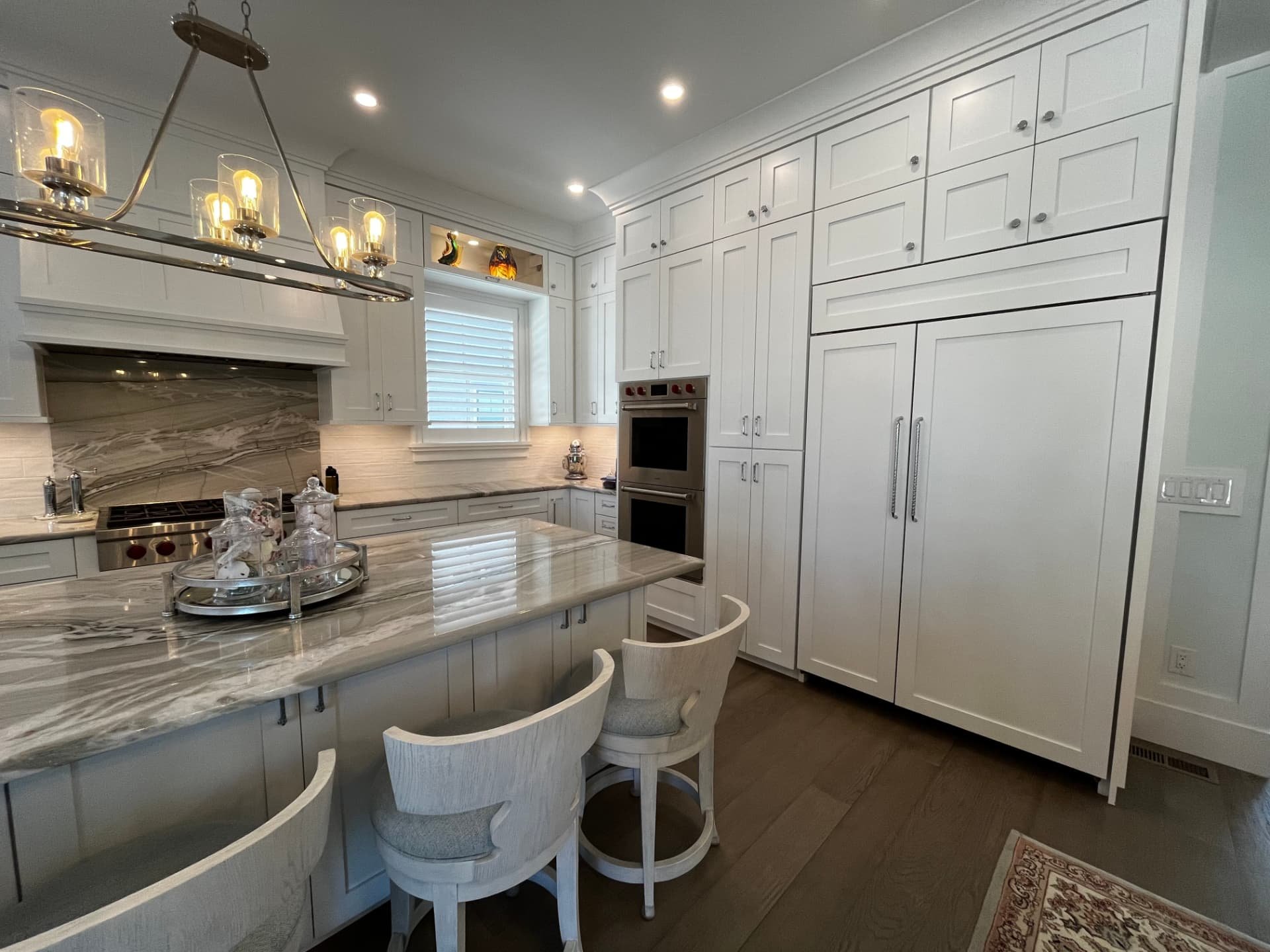 Floor-to-ceiling white shaker cabinetry with a paneled built-in refrigerator, double wall oven, and quartzite island